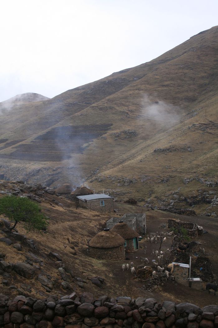 Stone huts amidst misty hills in a rural village, showcasing traditional thatched roofing.